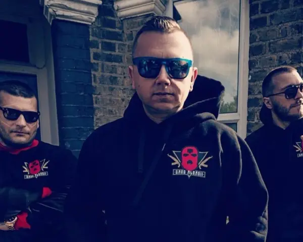 Trzech mężczyzn w bluzach z logo "Gang Albanii". Jeden z nich pokazuje gest ręką.