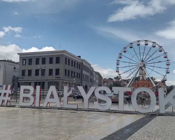 #Białystok - wielki napis zaprasza do odkrywania atrakcji miasta, w tle koło widokowe i zabytkowa zabudowa.