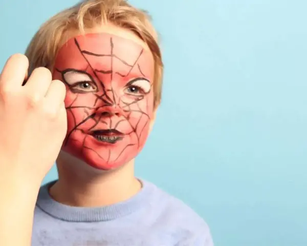 Ein Kind wird mit einem Spiderman-Gesicht bemalt. Rote Farbe und schwarze Spinnennetzmuster verwandeln das Gesicht in eine Superheldenmaske.
