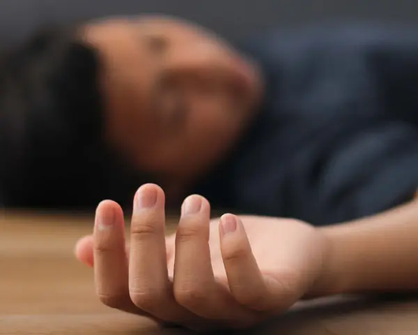 Nahaufnahme einer Hand, die auf dem Boden liegt, während eine Person mit einem epileptischen Anfall bewusstlos ist.