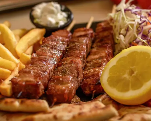 Pyszne souvlaki na patykach, podane z frytkami, pitą, surówką i cytryną.