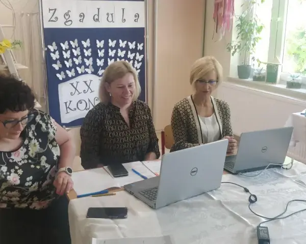 Trzy kobiety pracują przy stołach w sali, która wygląda jak szkoła specjalna. Na ścianie wisi tablica z motylami i napisem "Zgadula".