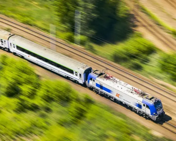 Pędzący pociąg PKP Intercity, model EU44 "Husarz", z białymi wagonami, mija zielone pola i drzewa.