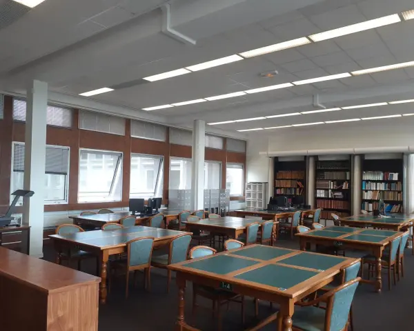 Salle de lecture avec tables, chaises et étagères de livres.