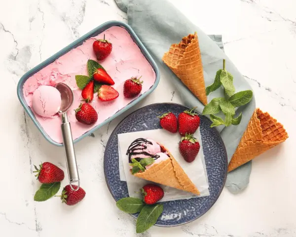 Ein Behälter mit rosa Obst Eis, Erdbeeren und Minze. Ein Eisbecher mit Eis und Schokoladensauce.