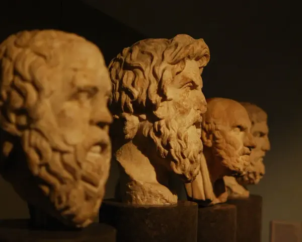 Bustos de mármol de filósofos de la edad antigua Grecia, con barbas y miradas serias, alineados en un museo.
