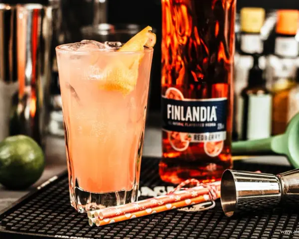 Orzeźwiające drinki z Finlandia Redberry, idealne na letnie wieczory. W szklance różowy koktajl z lodem i skórką cytrusową.