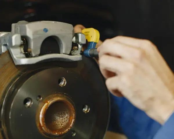 Mechanik dokręca śrubę w jarzmie zacisku hamulcowego, naprawiając układ hamulcowy pojazdu.