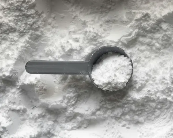 Miarka z białym proszkiem, prawdopodobnie disodium edta, na tle sypkiego materiału.