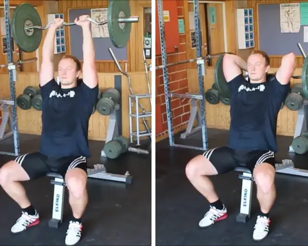 Man utför french press i gym. Han sitter på en bänk med en skivstång över huvudet, redo att sänka den bakom nacken.