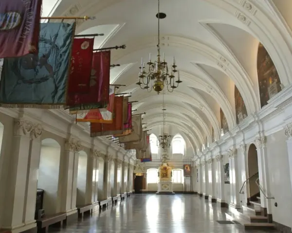 Długi korytarz z łukami i żyrandolami, ozdobiony historycznymi sztandarami. To wnętrze klasztoru na Jasnej Górze, gdzie każdy baner opowiada historię zakonu paulinów.