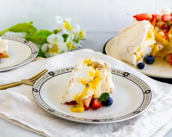 Porción de pavlova con fresas, arándanos y mango, bañada en salsa de maracuyá. Los pavlova ingredientes son visibles en este postre.