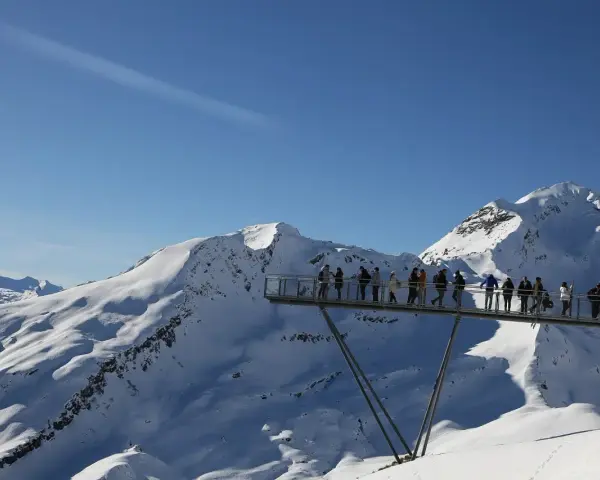 Ludzie na platformie widokowej podziwiają ośnieżone szczyty Alp, jakby byli w świecie Grindelwalda.