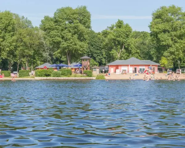 Sommerfreuden am See in Berlin: Menschen planschen im Wasser, entspannen am Strand und genießen die Sonne.