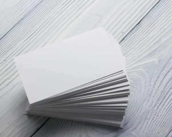 Stos białych wizytówek, idealnych na papier satynowy lub kredowy, leży na drewnianym blacie.