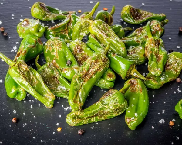 Friggitelli verdi, cotti in friggitrice ad aria, cosparsi di sale grosso e pepe nero su una superficie scura.
