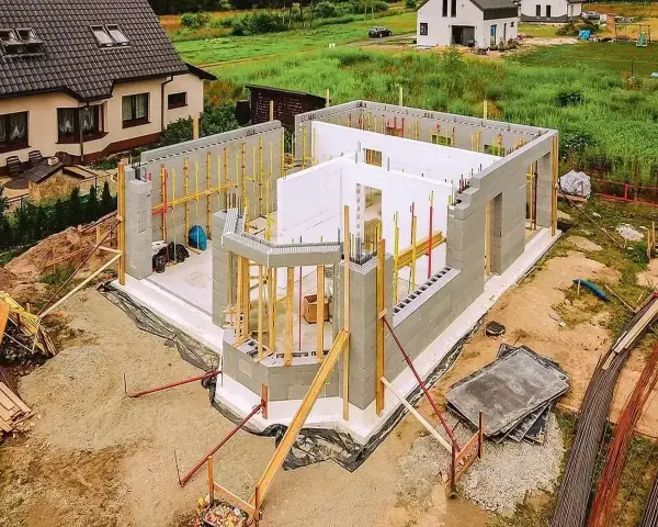 Budowa domu ze styropianu w toku. Ściany z bloczków betonowych i białego styropianu, zbrojenia i drewniane podpory.