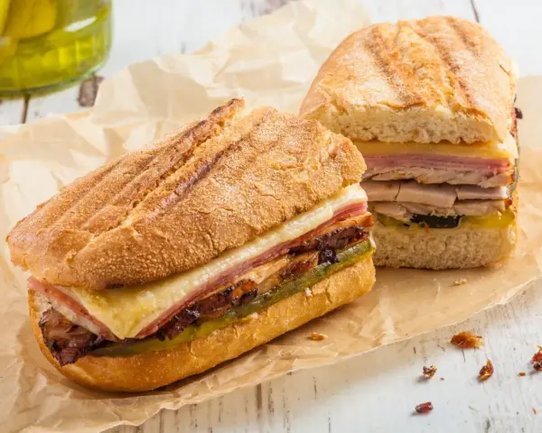Dos sándwiches cubanos a la parrilla con capas de carne, queso derretido y pepinillos.