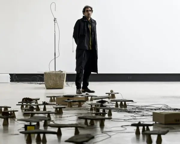 Tarek Atoui, artiste, se tient au milieu d'une installation sonore avec de nombreuses petites structures en pierre et en bois reliées par des câbles.