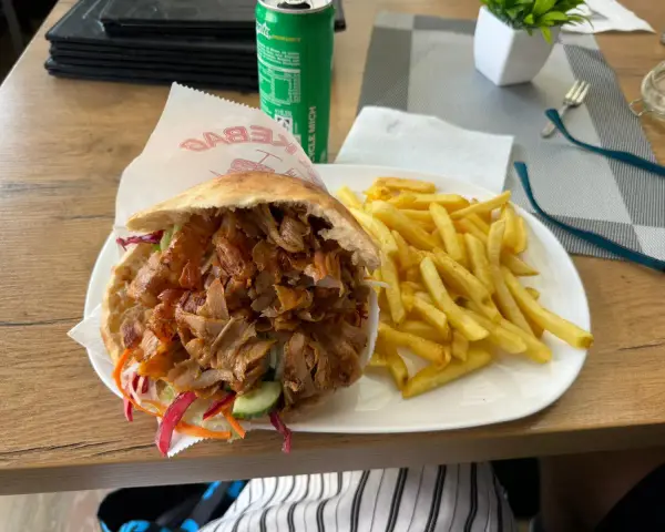 Kebab z frytkami na talerzu, obok puszka napoju.