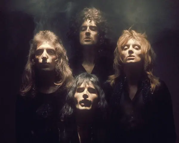 Czterech członków zespołu Queen w mrocznym klimacie, jakby przygotowujących się do wykonania "Bohemian Rhapsody". Ich spojrzenia sugerują głęboką interpretację.