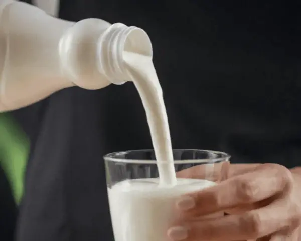 Kefir, naturalny probiotyk, pomaga zwalczać grzybicę jamy ustnej. Biały napój leje się z butelki do szklanki.