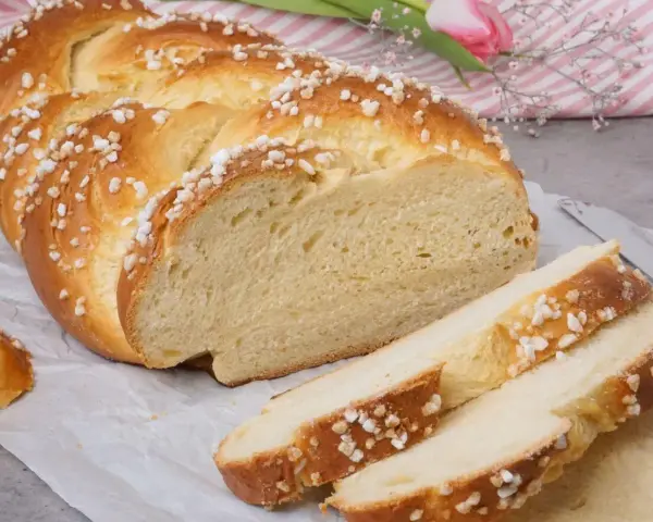 Ein goldbrauner Hefezopf, bestreut mit Zuckerkristallen, liegt auf Backpapier. Ein Stück ist angeschnitten, die weiche Krume ist sichtbar. Ein tolles Rezept für Hefezopf!