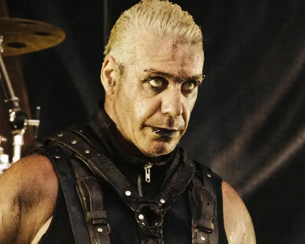 Till Lindemann młody, w skórzanym gorsecie, z mokrymi włosami i intensywnym spojrzeniem, gotowy do występu na scenie.