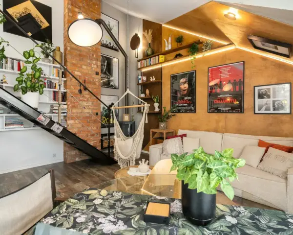 Wygodny salon w stylu loftowym z ceglaną ścianą, metalowymi schodami, wiszącym fotelem i dużą ilością zieleni.