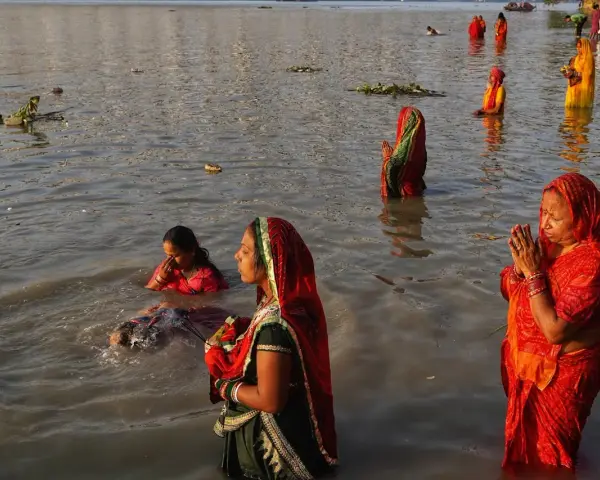 Mujeres rezan en el río Ganges, con vestimentas coloridas y el agua hasta la cintura.
