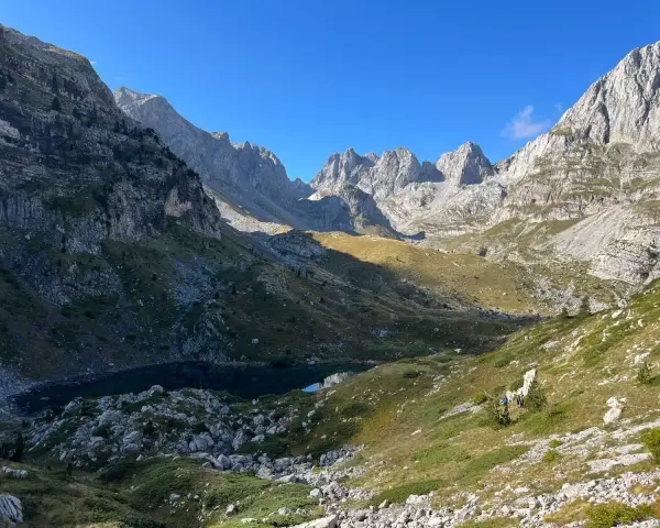 Majestatyczne, skaliste gory przeklete, z jeziorem w dolinie i turystami na szlaku.