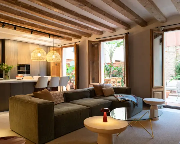 Sofá modular verde con acabado fratasado, mesas auxiliares, lámpara roja y acceso a patio con muebles de exterior.