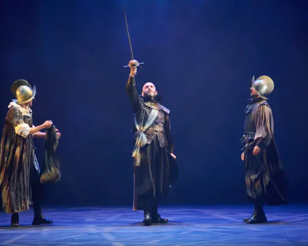 Tres hombres con armadura y espadas en un escenario. El del centro levanta su espada. Escena de "El alcalde de Zalamea".