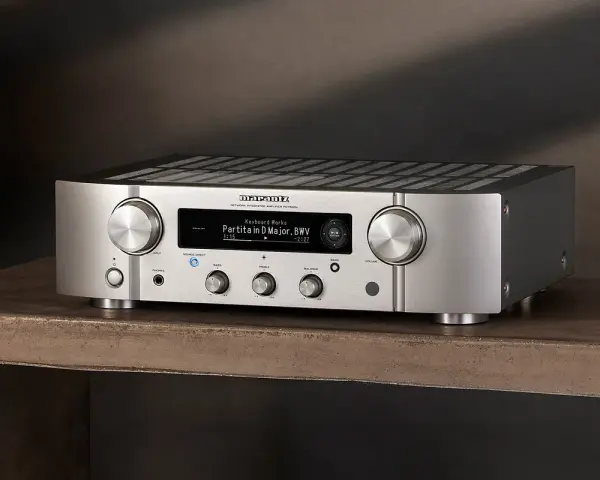 Srebrny wzmacniacz Marantz PM7000N, gotowy do testu, z wyświetlaczem pokazującym utwór muzyczny.