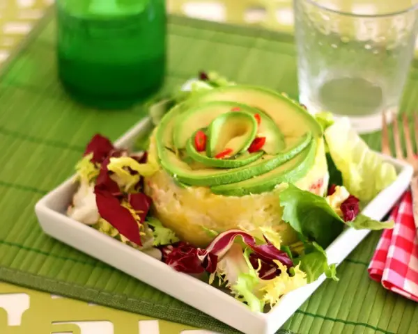 Causa limeña con aguacate en espiral y ensalada fresca, servida en plato blanco.
