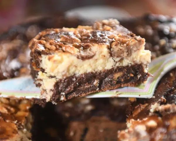 Ein Stück saftiger "friss dich dumm kuchen vom blech" mit Schichten aus Schokolade, Käsekuchen und Nüssen wird serviert.