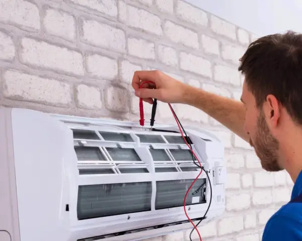 Sprawdź, jaka jest odgrzybianie klimatyzacji cena. Technik z miernikiem przy białej klimatyzacji.