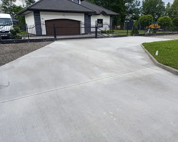 Nowy podjazd z betonu przed domem z garażem i bramą.