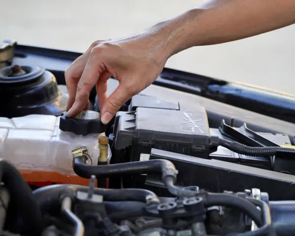 A hand twists the cap on a car's coolant reservoir, a step in learning how to dispose of antifreeze safely.
