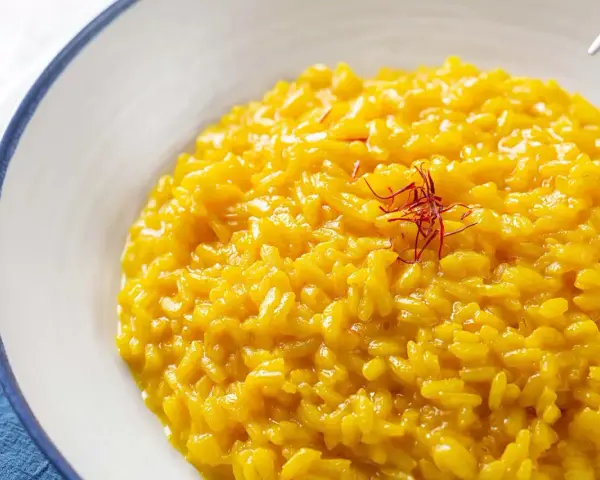 Un cremoso risotto alla milanese, giallo intenso grazie allo zafferano, guarnito con fili rossi.