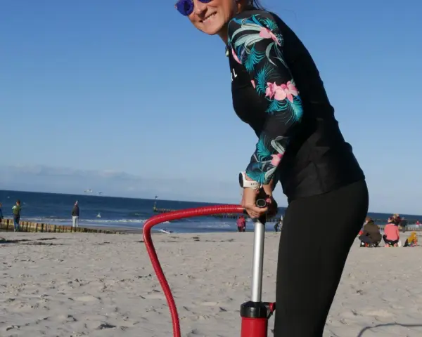 Frau pumpt SUP auf. Am Strand bereitet sie sich auf Wassersport vor.