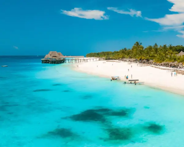 Rajskie plaże Zanzibaru w lutym. Turkusowa woda, biały piasek, palmy i urokliwy pomost z domkami na wodzie.
