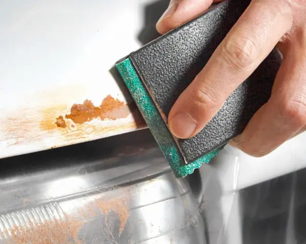 Sanding away rust on a car's bodywork. The abrasive block is removing the orange-brown corrosion.