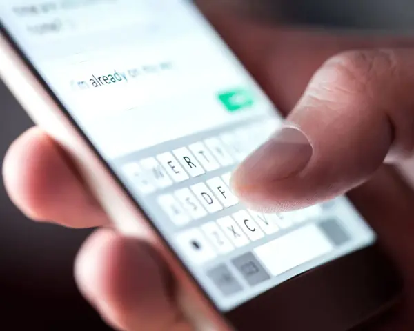 Palec pisze na klawiaturze telefonu: "Już w drodze na wesele!". Potwierdzenie przybycia na wesele sms.
