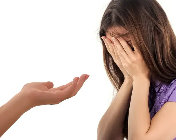 Kobieta płacze, zakrywając twarz dłońmi. Wyciągnięta dłoń oferuje wsparcie, symbolizując trudny moment, jak przyznać się do kłamstwa.