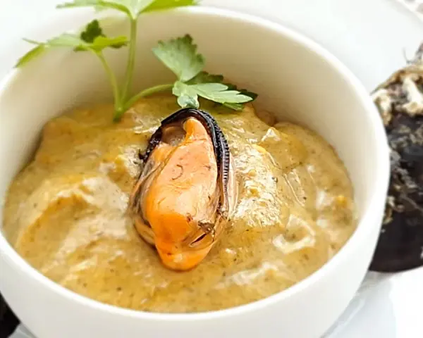 Paté de mejillones cremoso en cuenco blanco, decorado con perejil y mejillones enteros al lado.