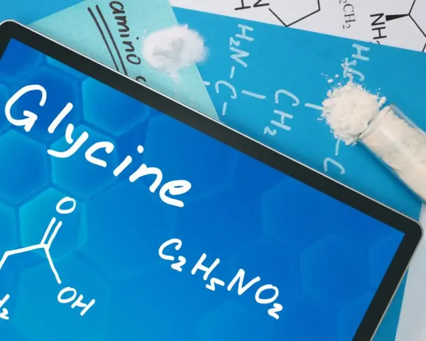 Tablet z napisem "Glycine", wzorem chemicznym i próbówką z proszkiem. Informacje o glicynie i jej dawkowanie.