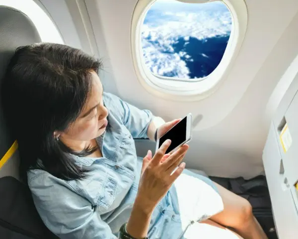 Kobieta z telefonem siedzi przy oknie w samolocie Ryanair, podziwiając widok chmur.