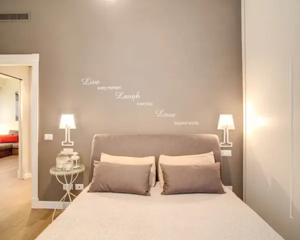 Camere da letto belle con citazione "Live, Laugh, Love" sulla parete. Letto accogliente con cuscini e lampade moderne.