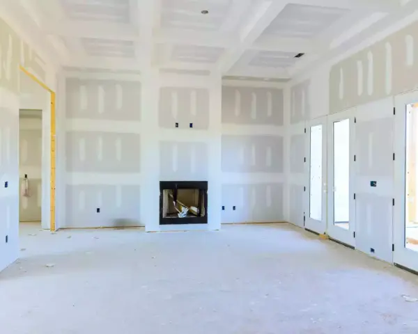 Interno di una casa in costruzione con pareti e soffitto in cartongesso, camino e porte a doppio battente.